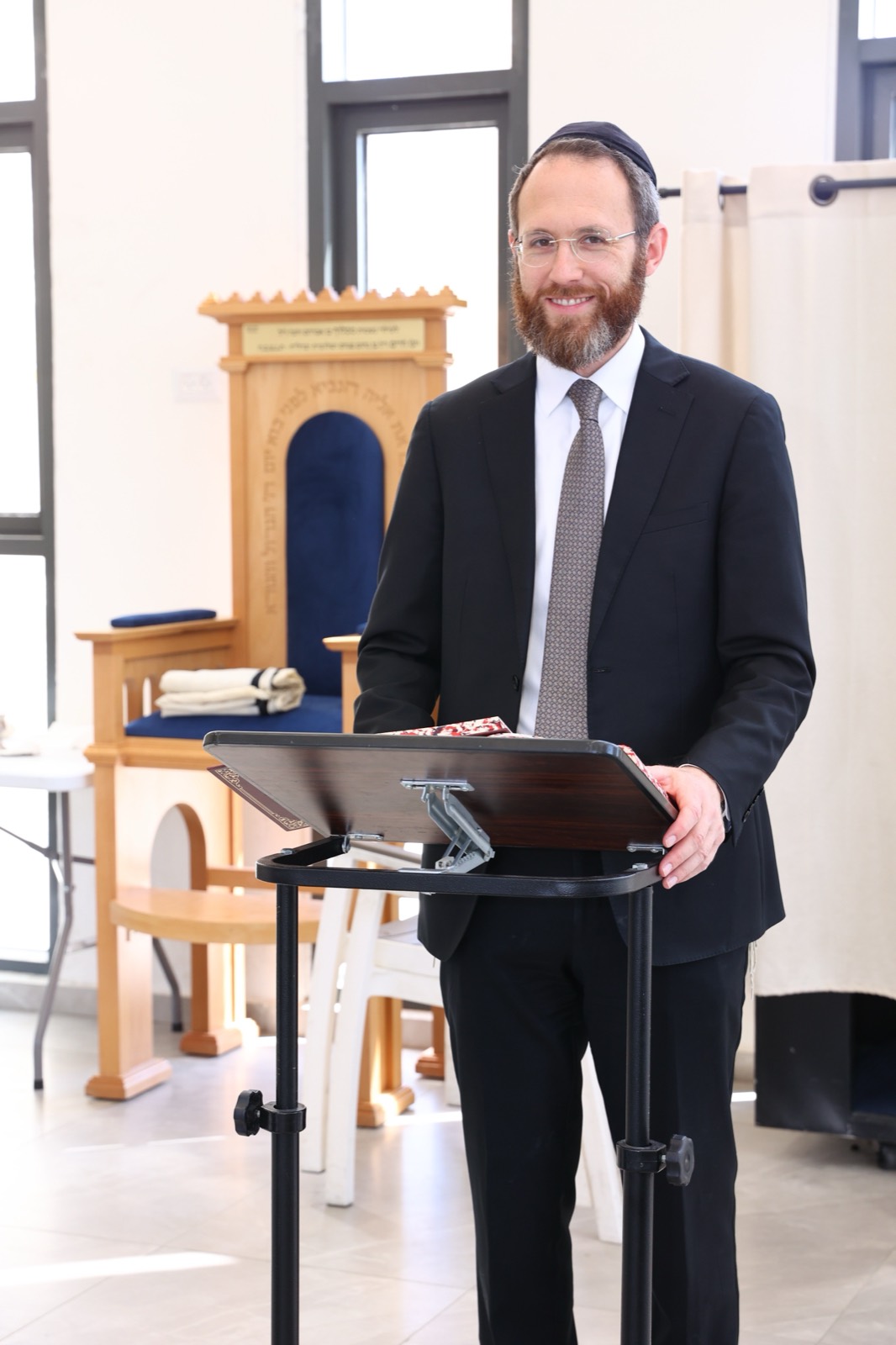Rabbi Grossman delivering remarks at a podium in a beit knesset